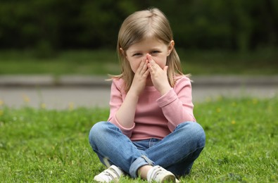 Photo of Little girl suffering from seasonal spring allergy on green grass in park