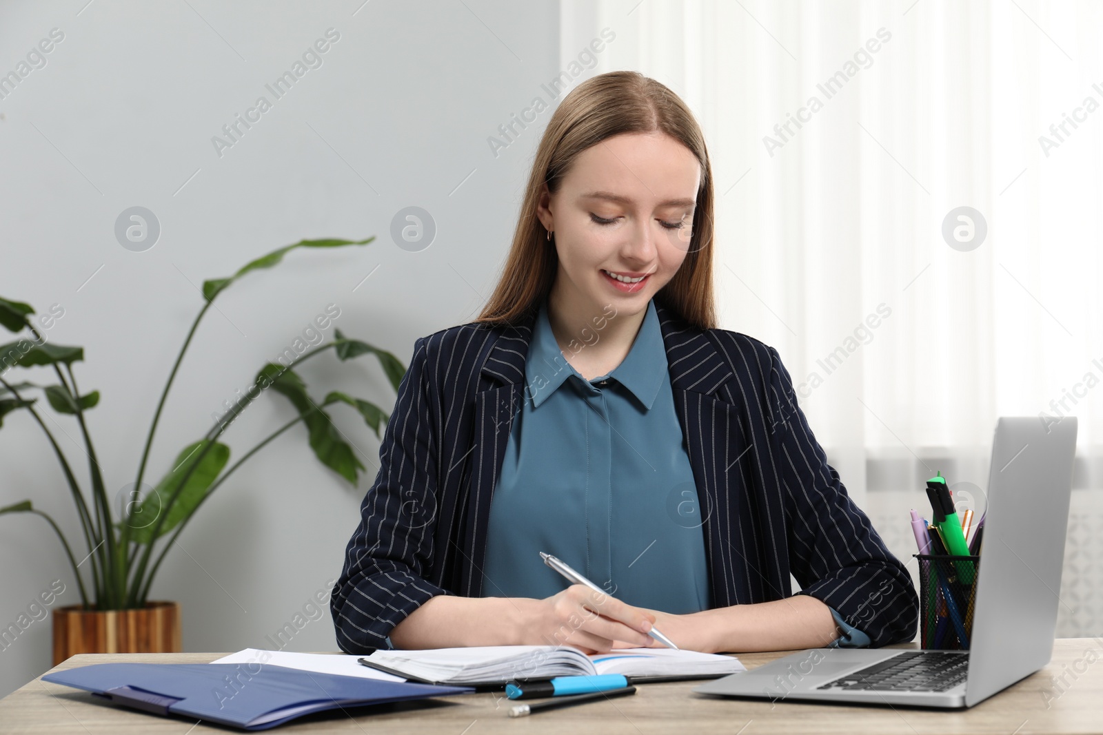 Photo of Woman taking notes at wooden table in office