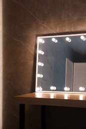 Modern mirror with light bulbs on wooden table in room