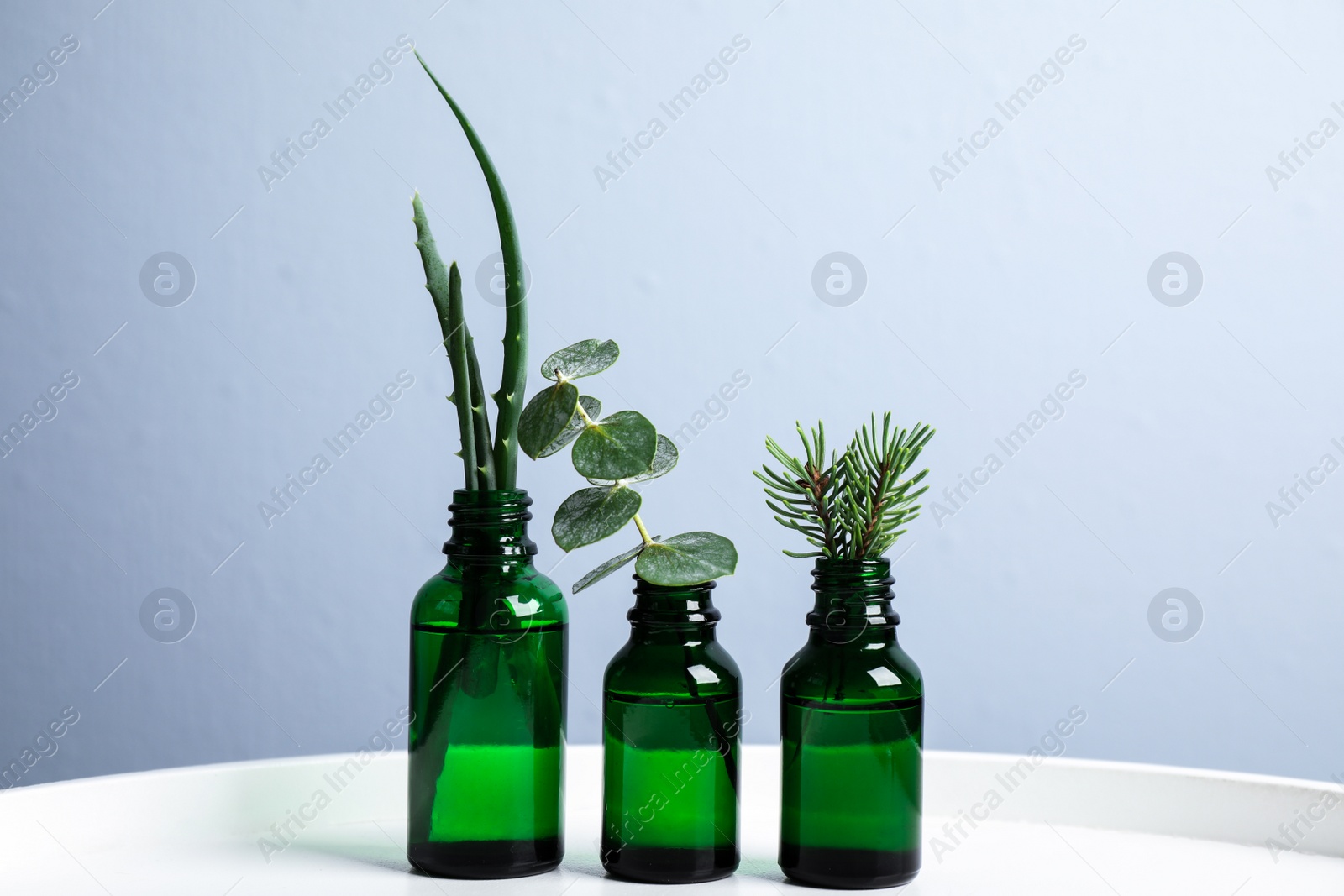 Photo of Glass bottles of different essential oils with plants on table