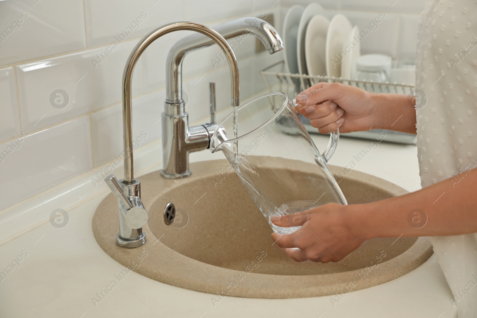 Photo of Woman pouring water into glass jug in kitchen, closeup