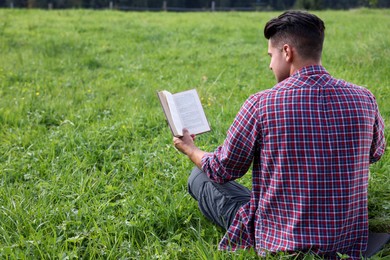 Man reading book on green grass, back view