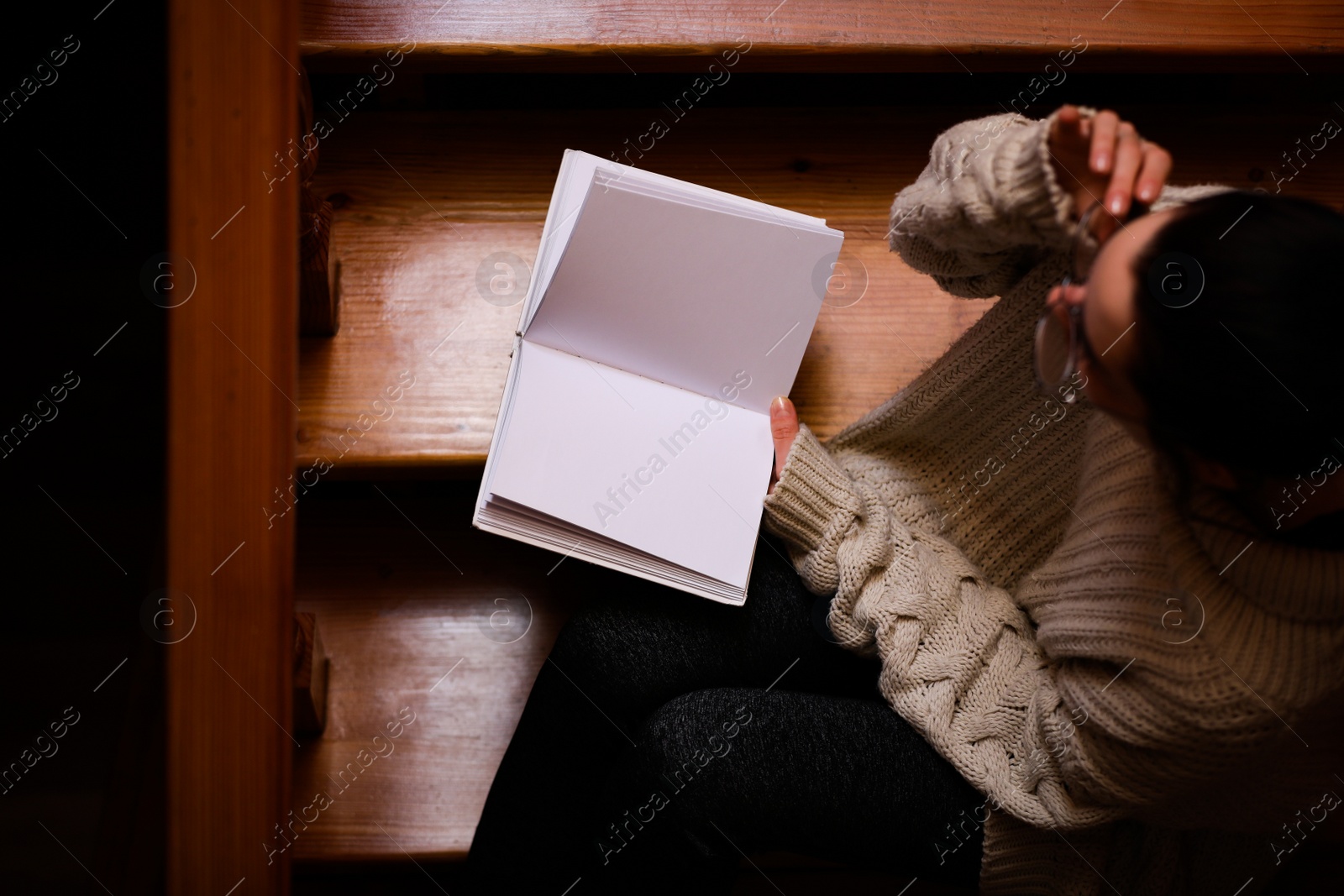 Photo of Woman reading book on wooden staircase, view from above