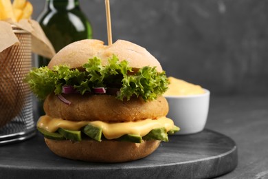 Photo of Tasty vegetarian burger with cutlet, cheese, avocado and onion on black table, closeup. Space for text