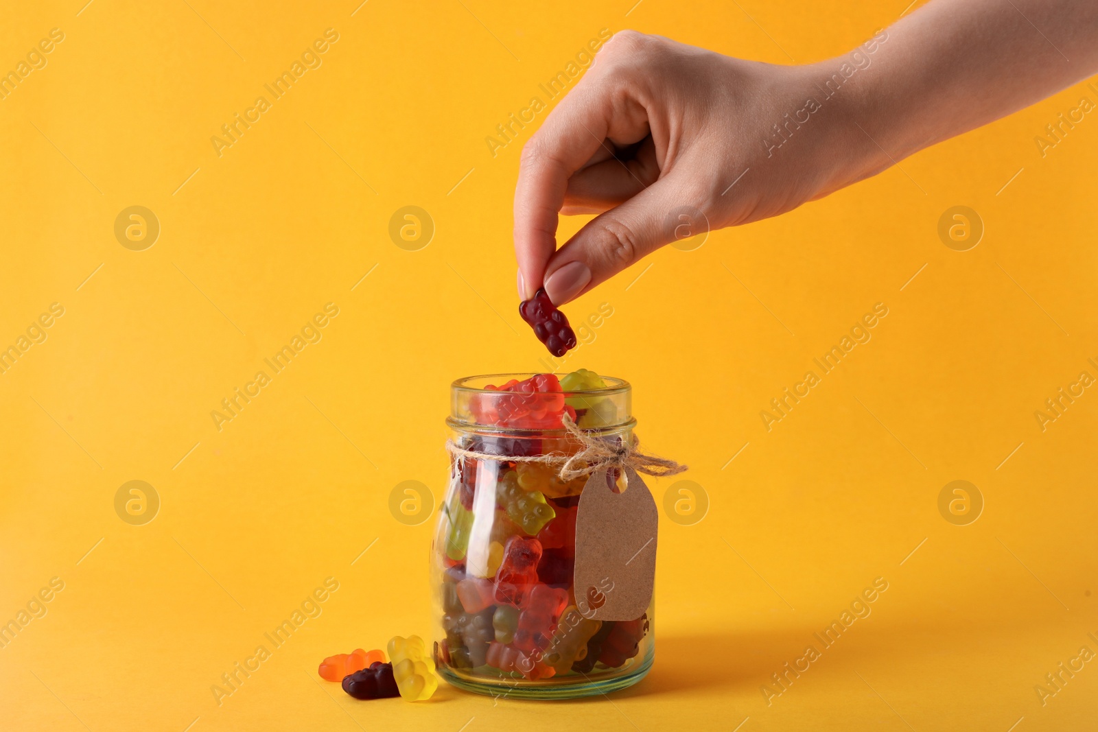 Photo of Woman taking gummy bear candy from glass jar on yellow background, closeup