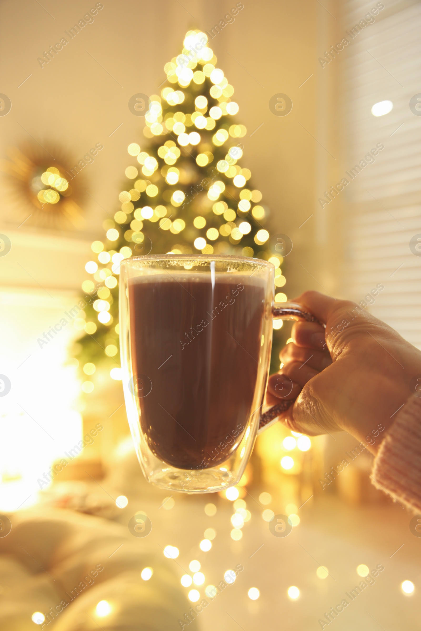 Photo of Woman with cup of drink and blurred Christmas tree on background, closeup