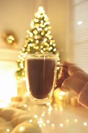Photo of Woman with cup of drink and blurred Christmas tree on background, closeup