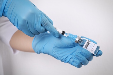 Doctor filling syringe with vaccine against Covid-19 on white background, closeup