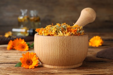 Photo of Mortar of dry calendula and fresh flowers on wooden table