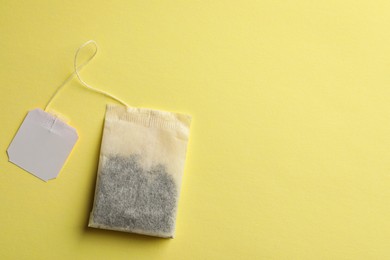 Photo of Paper tea bag with tag on yellow background, top view. Space for text