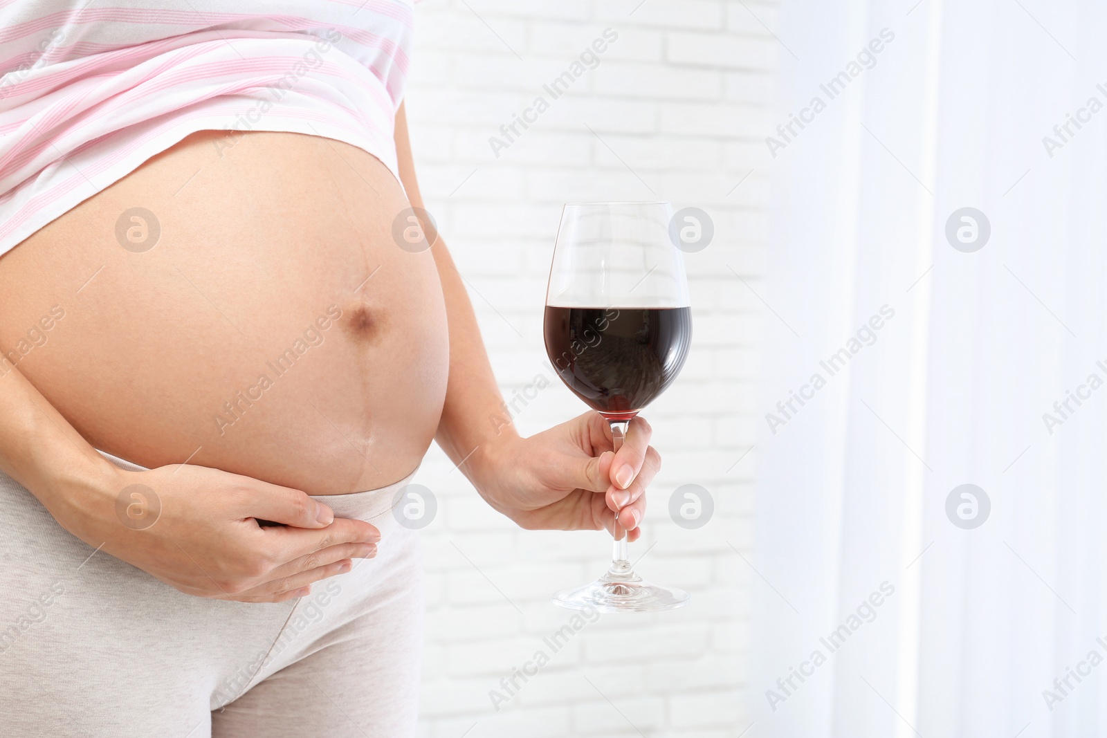 Photo of Pregnant woman with glass of red wine indoors, space for text. Alcohol addiction