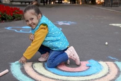 Happy child drawing rainbow with chalk on asphalt