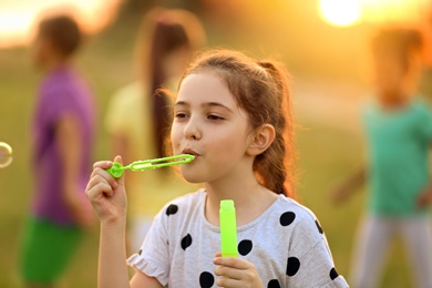 Image of Cute little girl blowing soap bubbles outdoors at sunset