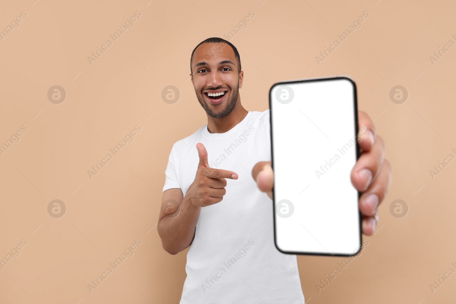 Photo of Young man showing smartphone in hand and pointing at it on beige background