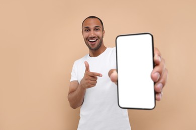 Young man showing smartphone in hand and pointing at it on beige background