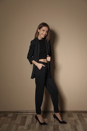 Full length portrait of beautiful young woman in fashionable suit near beige wall indoors. Business attire