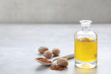 Photo of Bottle of nutmeg oil, nuts and powder on light grey table, space for text