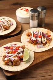 Photo of Delicious tacos with vegetables, meat and sauce on wooden table