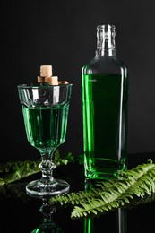 Photo of Absinthe, brown sugar, spoon and green leaves on mirror table. Alcoholic drink