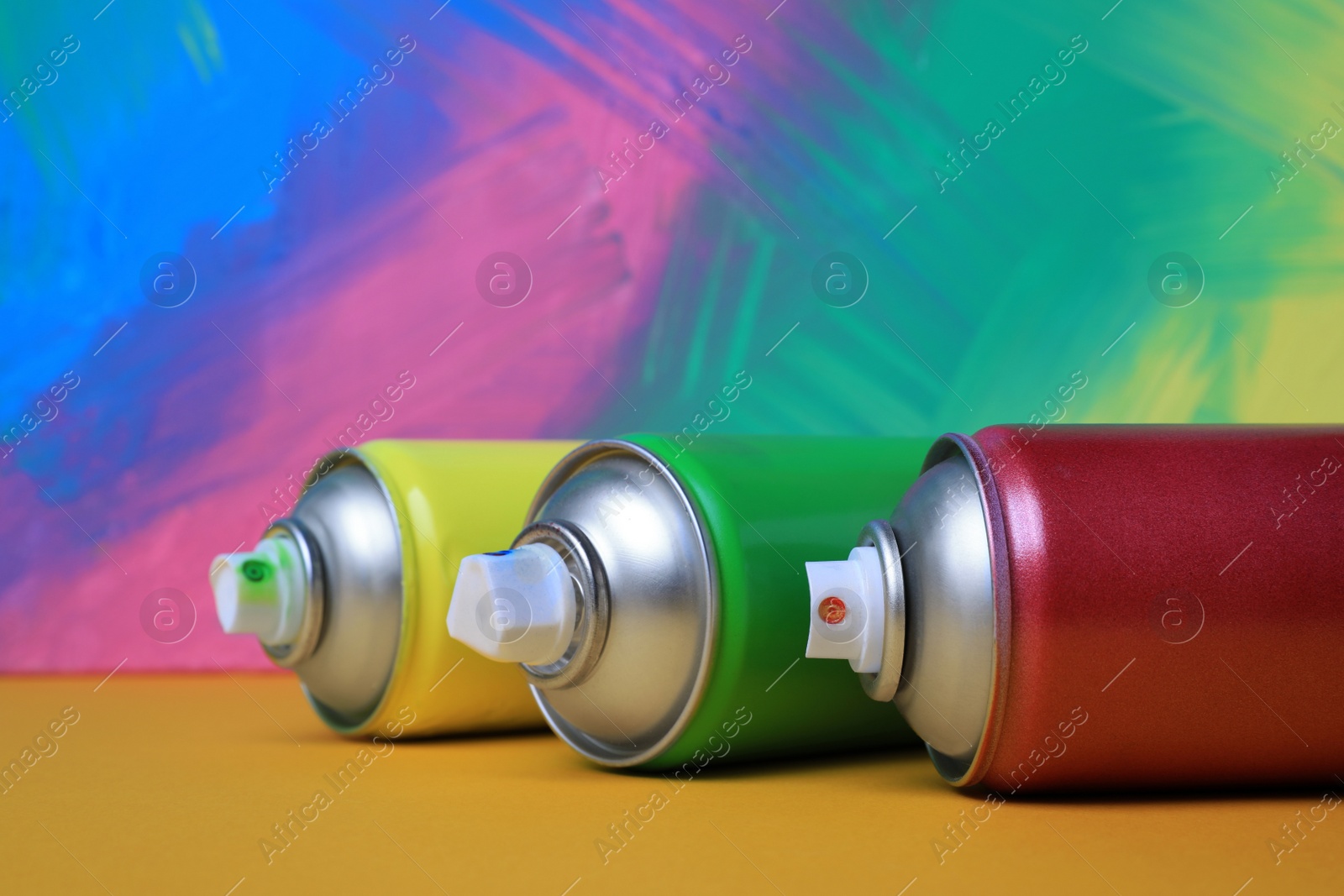 Photo of Cans of different spray paints on color background, closeup. Graffiti supplies