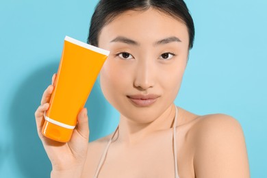 Photo of Beautiful young woman holding sun protection cream on light blue background