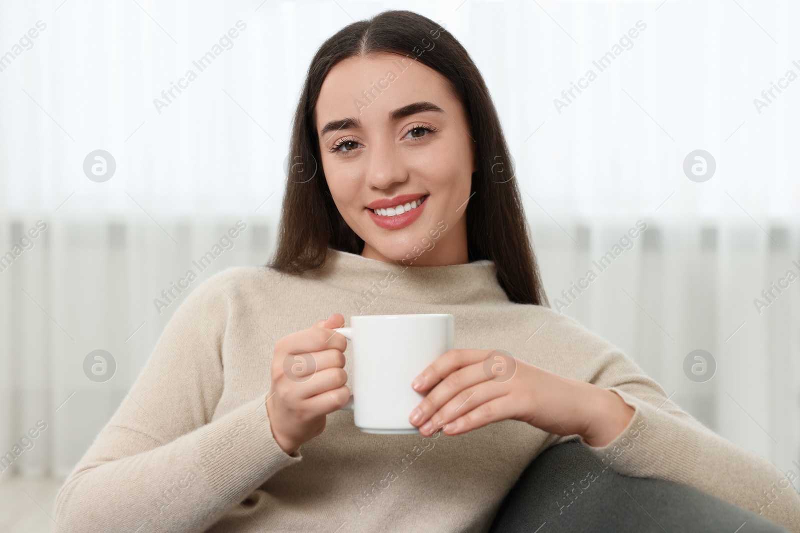 Photo of Happy young woman holding white ceramic mug at home