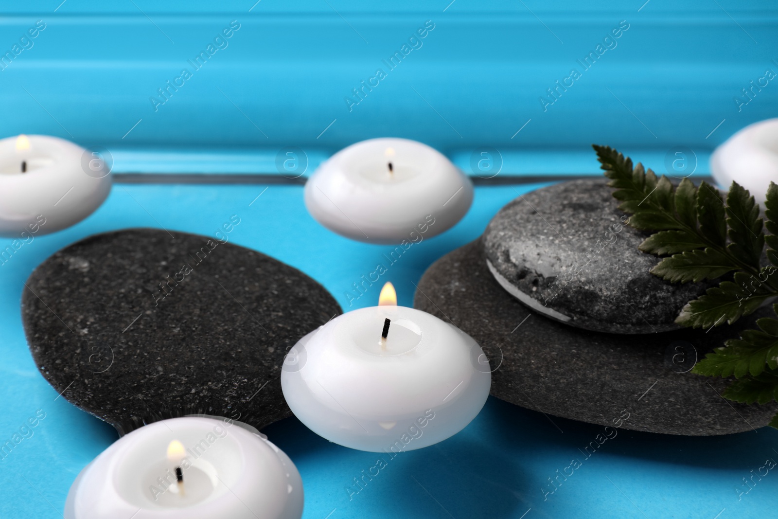Photo of Burning candles, green leaf and spa stones in water