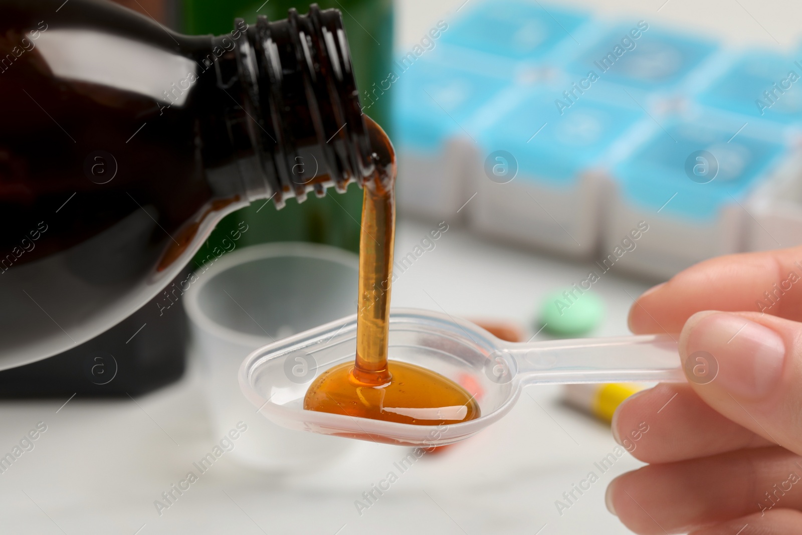 Photo of Woman pouring syrup from bottle into dosing spoon against blurred background, closeup. Cold medicine