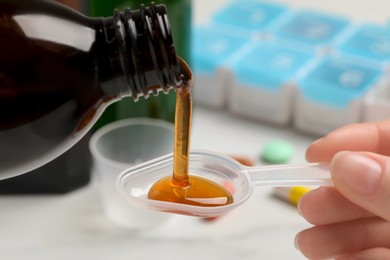 Photo of Woman pouring syrup from bottle into dosing spoon against blurred background, closeup. Cold medicine
