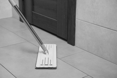 Photo of Cleaning grey tiled floor with mop near door