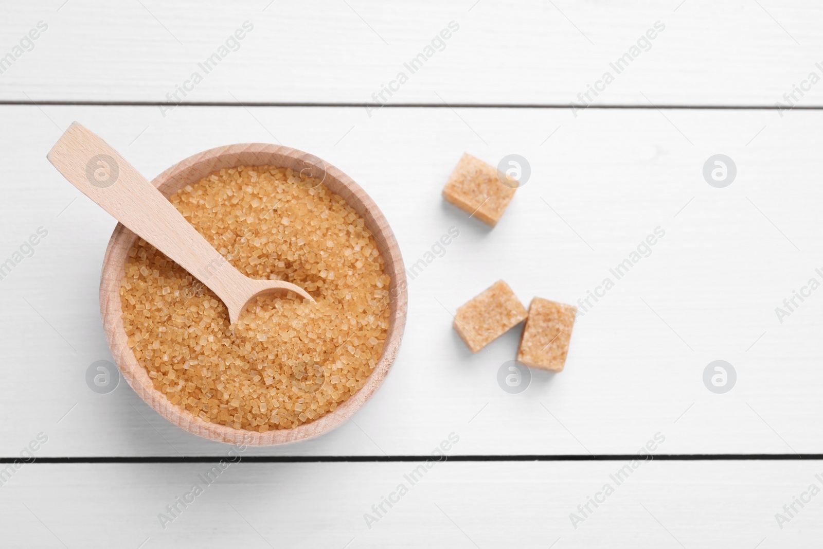 Photo of Bowl and spoon with brown sugar on white wooden table, top view. Space for text