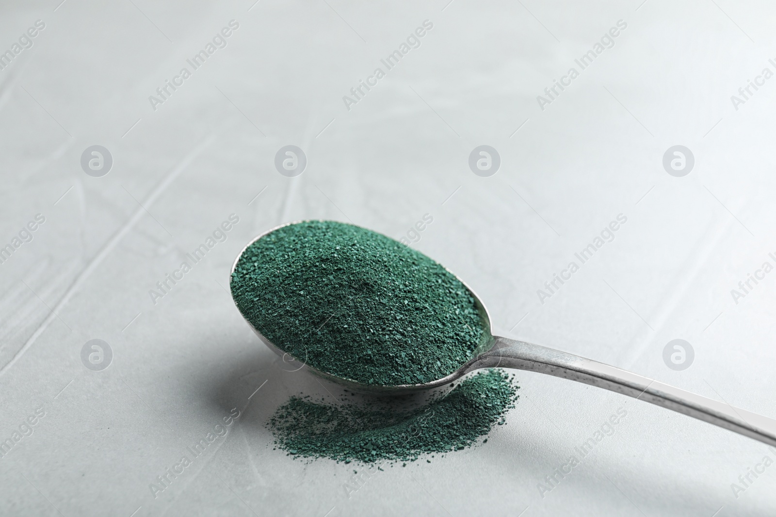 Photo of Spoon of spirulina algae powder on grey background