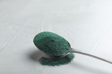 Photo of Spoon of spirulina algae powder on grey background