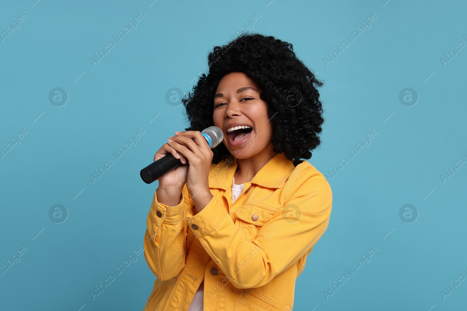 Photo of Beautiful woman with microphone singing on light blue background