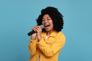 Beautiful woman with microphone singing on light blue background