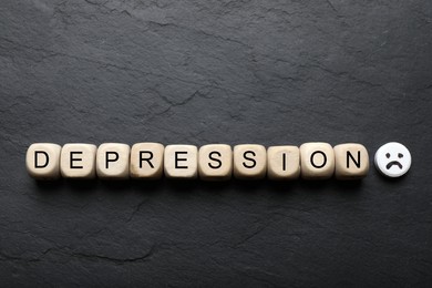 Photo of Word Depression made of wooden cubes and pill with sad face on black table, flat lay