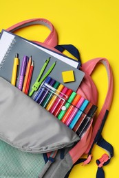 Photo of Backpack with school stationery on yellow background, top view