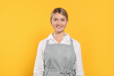 Photo of Beautiful young woman in clean apron with pattern on orange background