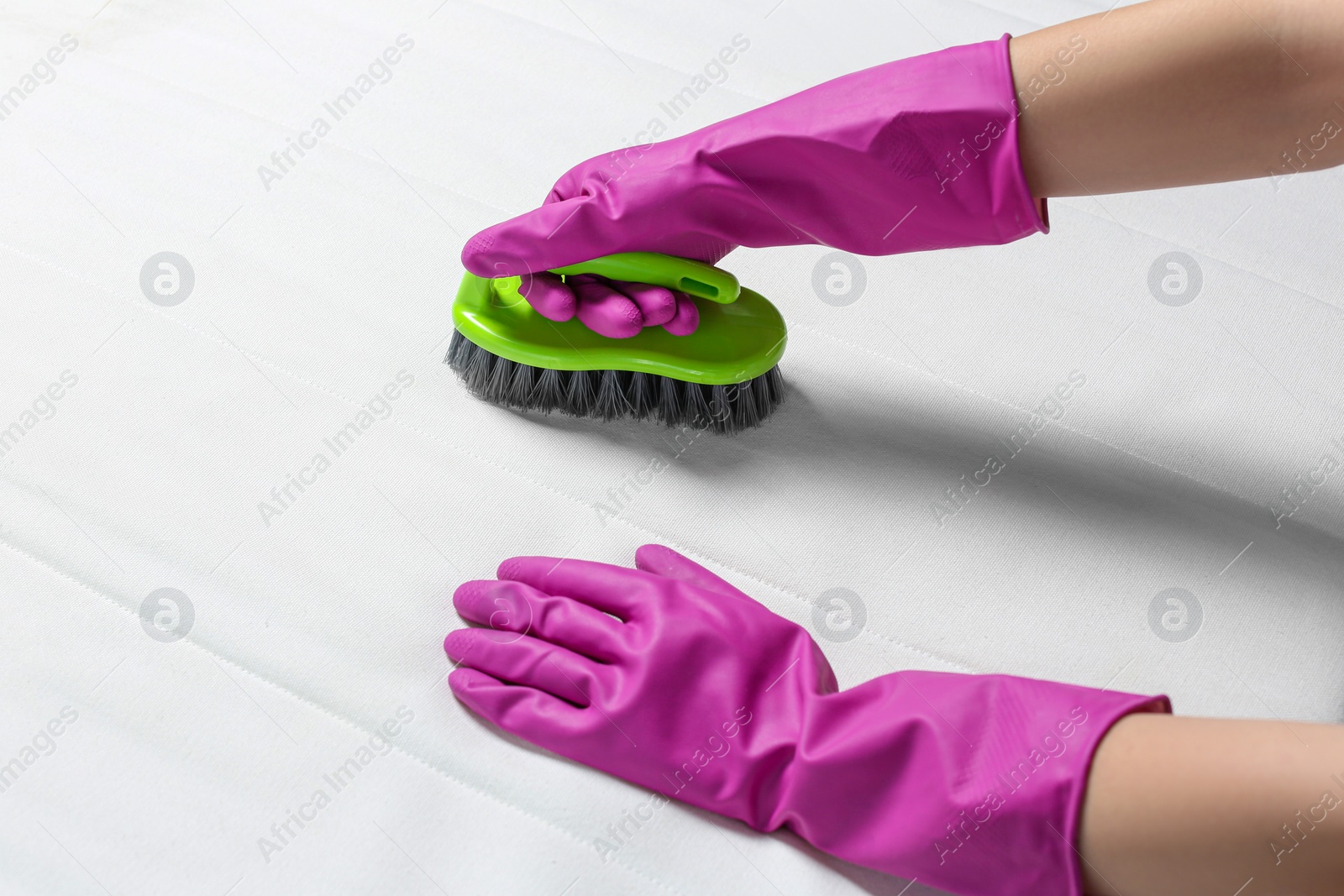 Photo of Woman in purple gloves cleaning white mattress with brush, closeup