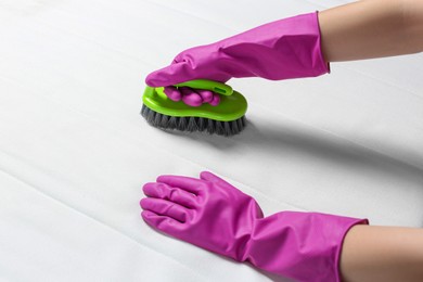 Woman in purple gloves cleaning white mattress with brush, closeup