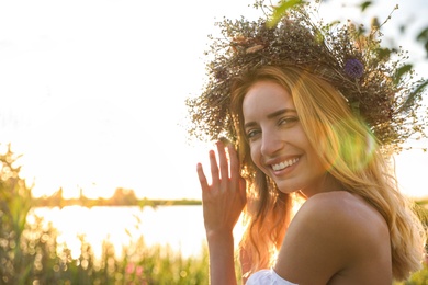 Young woman wearing wreath made of beautiful flowers outdoors on sunny day