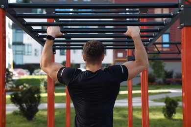 Photo of Man training on monkey bars at outdoor gym, back view