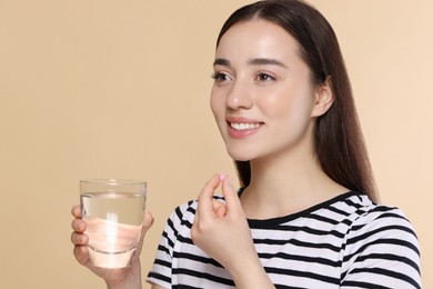 Photo of Happy woman with glass of water taking pill on beige background