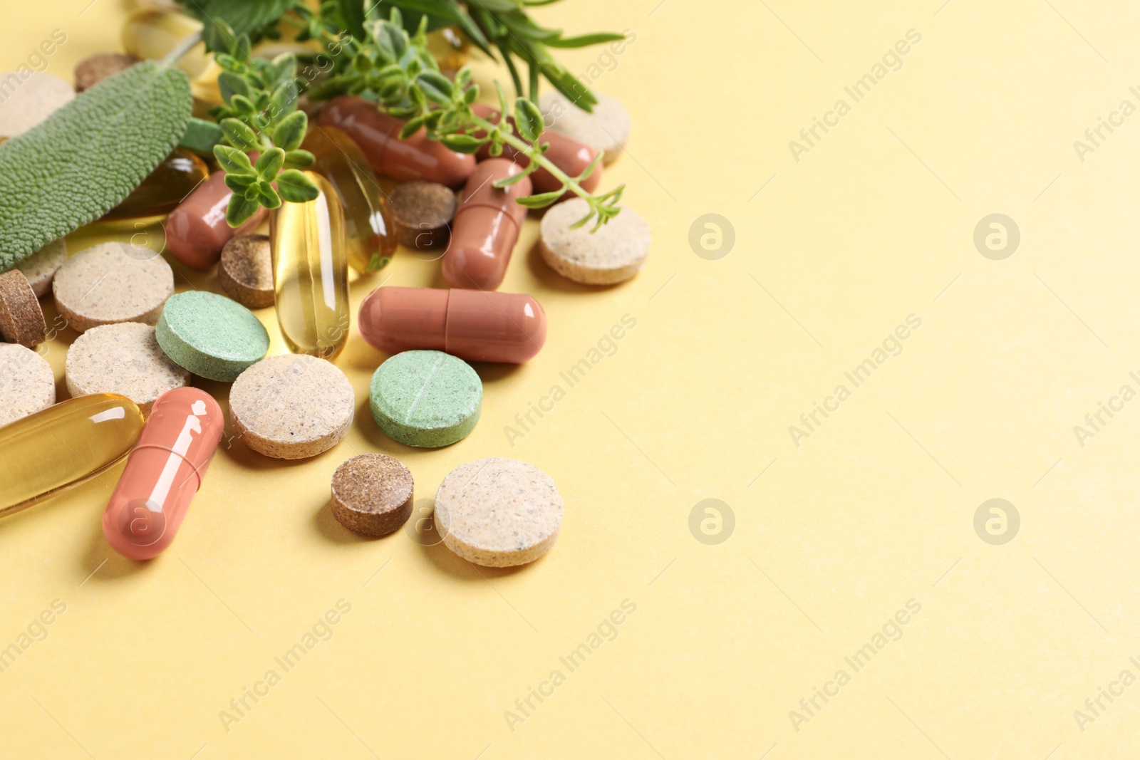 Photo of Different pills and herbs on light yellow background, space for text. Dietary supplements