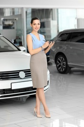 Photo of Young saleswoman with clipboard in car dealership