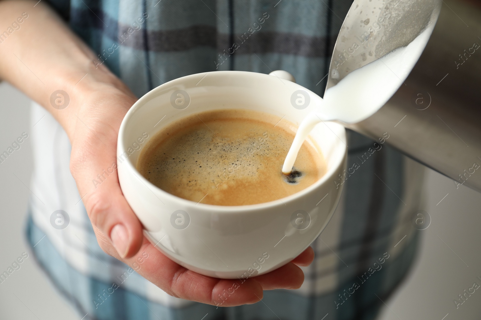 Photo of Woman pouring milk into cup of hot coffee, closeup