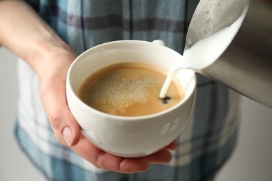 Woman pouring milk into cup of hot coffee, closeup