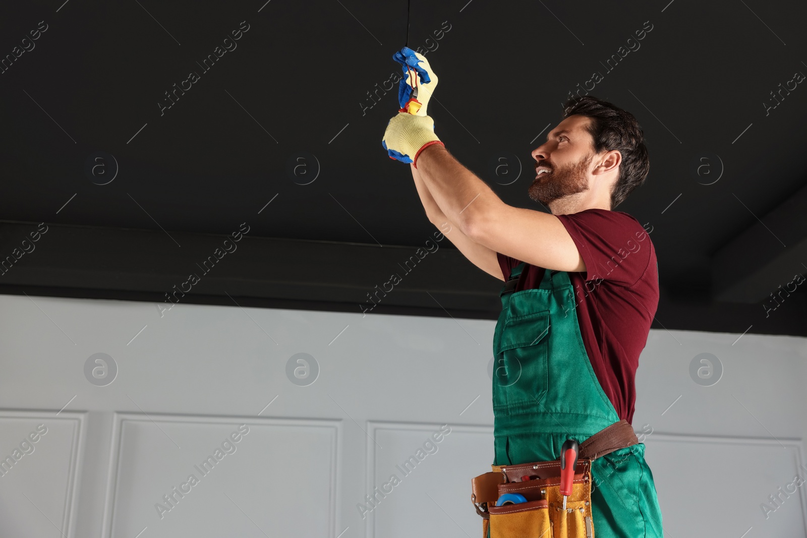 Photo of Electrician with pliers repairing ceiling wiring indoors