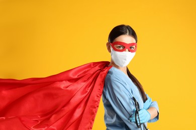 Photo of Doctor dressed as superhero posing on yellow background. Concept of medical workers fighting with COVID-19
