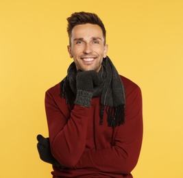 Photo of Happy young man in warm clothes on yellow background. Winter season